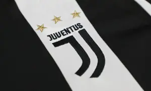 Zbliżenie na herb Juventusu z trzema złotymi gwiazdkami i napisem "JUVENTUS" na tle charakterystycznych czarno-białych pasów.