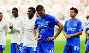 Piłkarze Bayer Leverkusen w niebieskich strojach, w tym z numerami 14 i 30, czekają na boisku. Czekamy na nowe bayer leverkusen transfery.