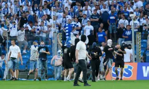 Kibice Lecha Poznań w niebiesko-białych barwach, niektórzy w kominiarkach, na murawie stadionu.