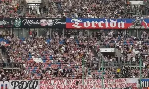 Trybuny stadionu wypełnione kibicami. Na banerach widnieje napis "Torcida" i nazwiska zawodników.