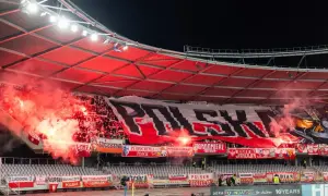 Kibice na stadionie odpalają race, tworząc czerwony dym. Na trybunach rozwinięty ogromny transparent "POLSKA" i flagi.