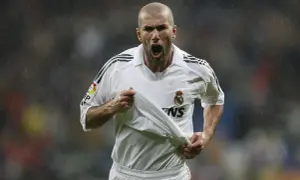 Zinedine Zidane w białej koszulce Realu Madryt, z podniesioną koszulką, krzyczy radośnie do kibiców.