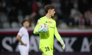 Młody bramkarz Wisły Kraków w neonowożółtej koszulce z numerem 28 trzyma piłkę.