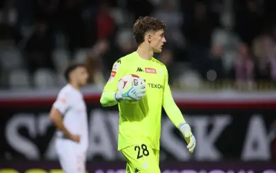 Młody bramkarz Wisły Kraków w neonowożółtej koszulce z numerem 28 trzyma piłkę.