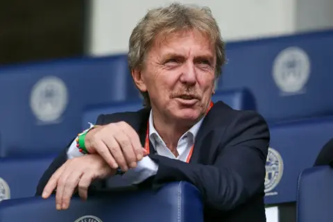 Zbigniew Boniek, żyje i ma się dobrze, siedzi na trybunach w garniturze, z charakterystycznymi wąsami.