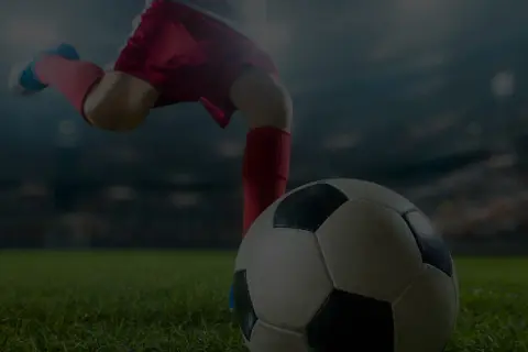 Noga piłkarza w czerwonych spodenkach i getrach kopie piłkę na tle stadionu. Nawet starzy piłkarze potrafią wzbudzić emocje.
