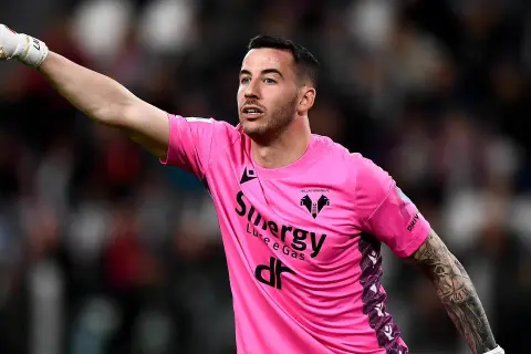 Bramkarz w różowej koszulce Hellas Verona wskazuje palcem, jakby chciał wiedzieć, ile trwa dogrywka w piłce nożnej.