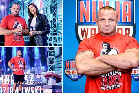 Mariusz Pudzianowski w czerwonej koszulce z napisem "Skóry nie sprzedam" na tle toru Ninja Warrior. Czy Mariusz Pudzianowski ma żonę? To pytanie nurtuje fanów.