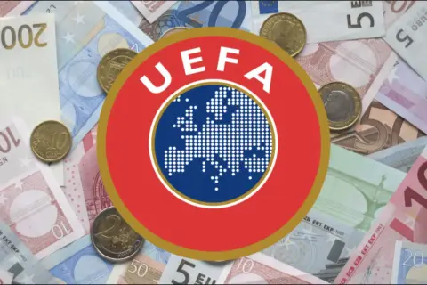 Logo UEFA na tle banknotów i monet euro. Symbolizuje finansowe fair play w europejskiej piłce nożnej.