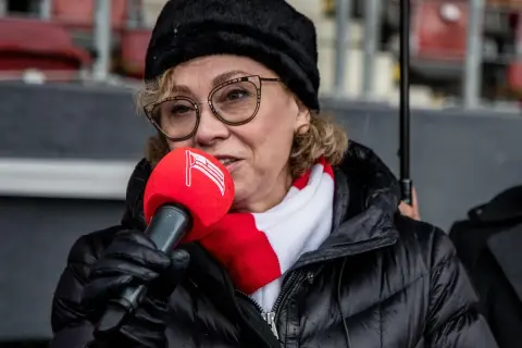 Prezes Cracovii w czapce i szaliku klubu, z mikrofonem w ręku, przemawia do zgromadzonych.