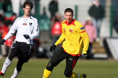 Młody Lewandowski w żółtej koszulce, jeszcze przed erą Legii Warszawa, walczy o piłkę na boisku.