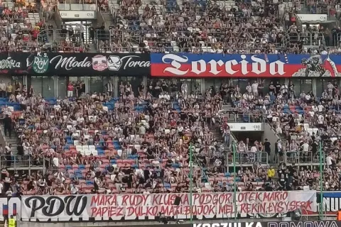 Trybuny stadionu wypełnione kibicami. Na banerach widnieje napis "Torcida" i nazwiska zawodników.