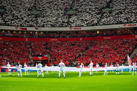 Piłkarze z flagą Polski na murawie, kibice tworzą biało-czerwone morze. Polska w rankingu FIFA zajmuje wysokie miejsce, co widać po dumie na trybunach.