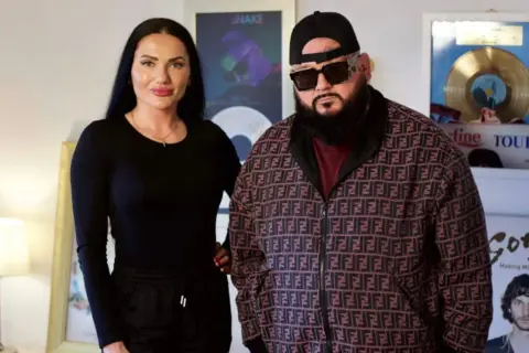 Ewa Brodnicka i jej partner pozują do zdjęcia. Ona w czarnej bluzce, on w charakterystycznej kurtce z logo.