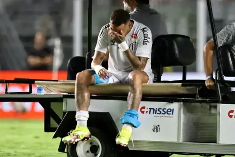 Neymar siedzi na wózku golfowym, trzymając się za twarz. Wygląda na to, że doznał kontuzji, która uniemożliwia mu dalszą grę.