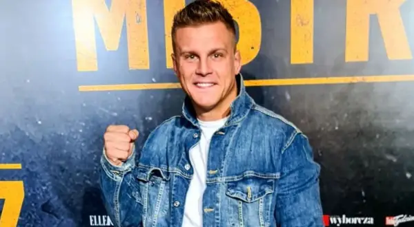 Uśmiechnięty Alan Kwieciński, którego wiek jest często przedmiotem dyskusji, w jeansowej kurtce.