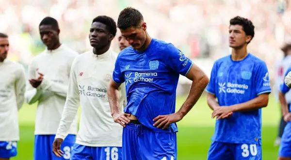 Piłkarze Bayer Leverkusen w niebieskich strojach, w tym z numerami 14 i 30, czekają na boisku. Czekamy na nowe bayer leverkusen transfery.