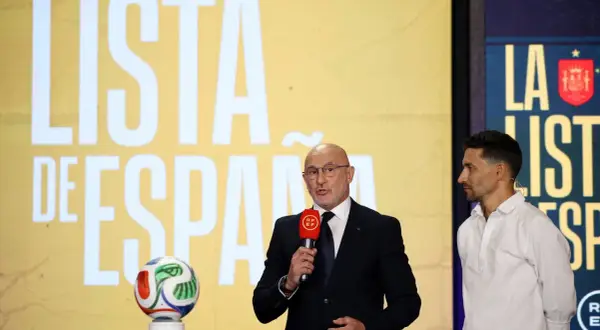 Mężczyzna w garniturze ogłasza hiszpania powołania, obok stoi piłkarz. Na ekranie w tle napis "LISTA DE ESPAÑA".