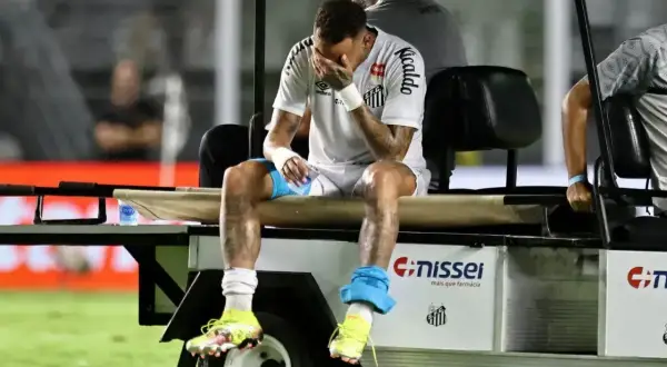 Neymar siedzi na wózku golfowym, trzymając się za twarz. Wygląda na to, że doznał kontuzji, która uniemożliwia mu dalszą grę.