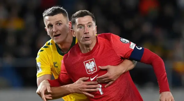 Robert Lewandowski, kapitan Polski, w czerwonej koszulce z orłem, walczy o piłkę z przeciwnikiem.