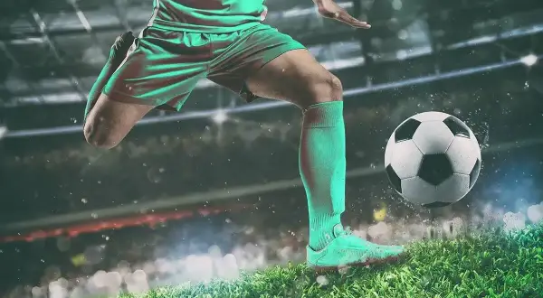 Piłkarz w akcji, jak legenda futbolu, kopie piłkę na tle stadionu.
