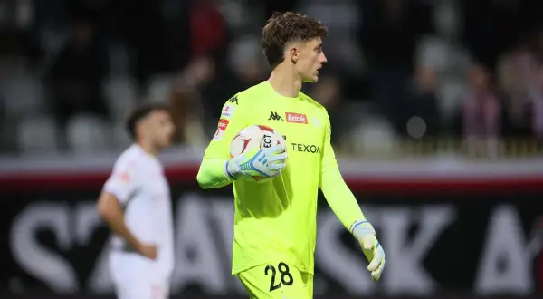 Młody bramkarz Wisły Kraków w neonowożółtej koszulce z numerem 28 trzyma piłkę.