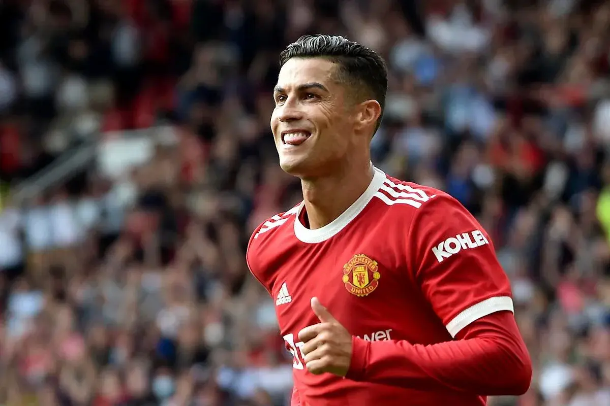 Cristiano Ronaldo w czerwonej koszulce Manchesteru United, z charakterystyczną fryzurą 2023, pokazuje kciuk w górę i wystawia język.