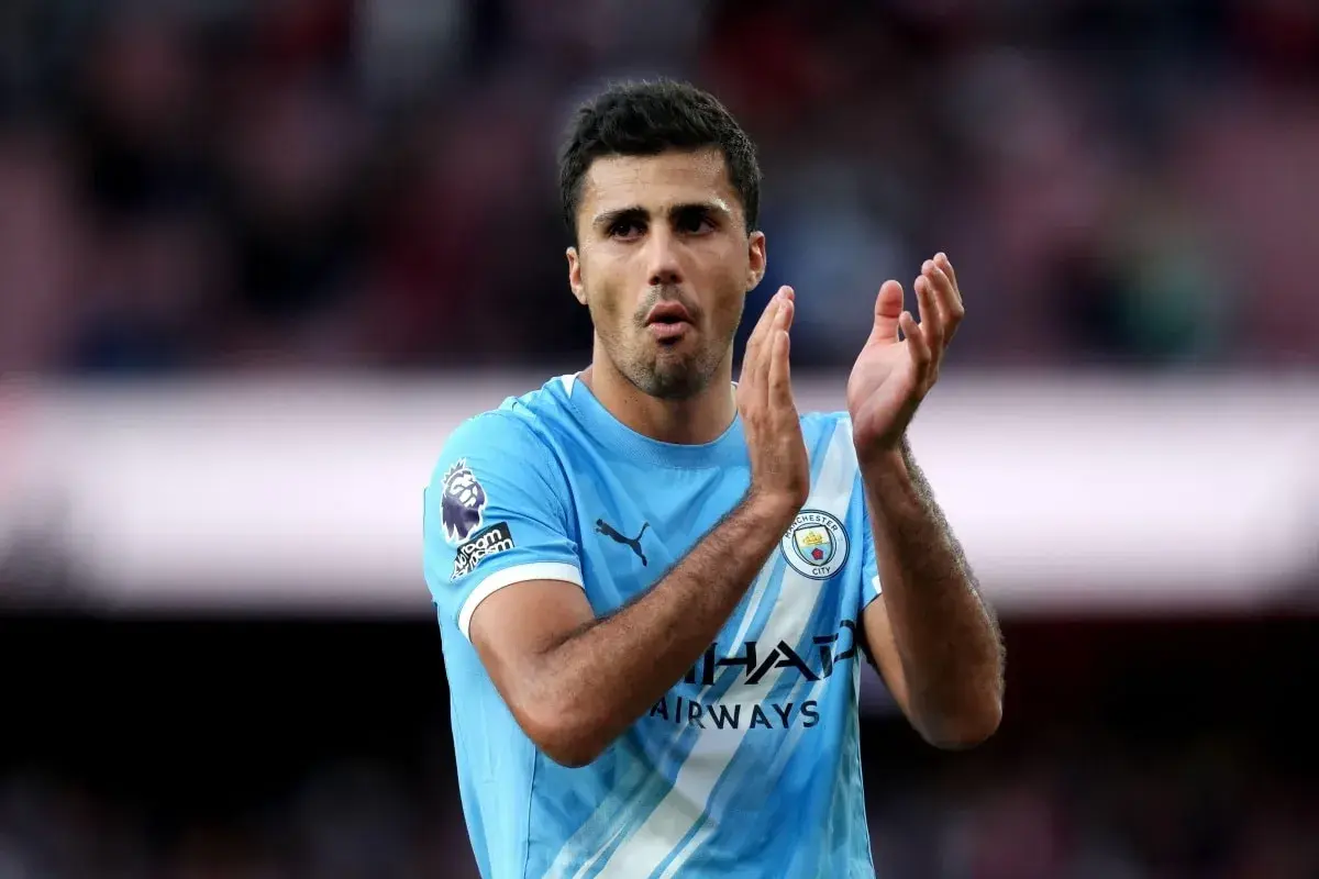 Piłkarz Manchesteru City w błękitnej koszulce z herbem klubu, klaszczący. Jego obecność budzi nadzieję na kolejne udane manchester city transfery.