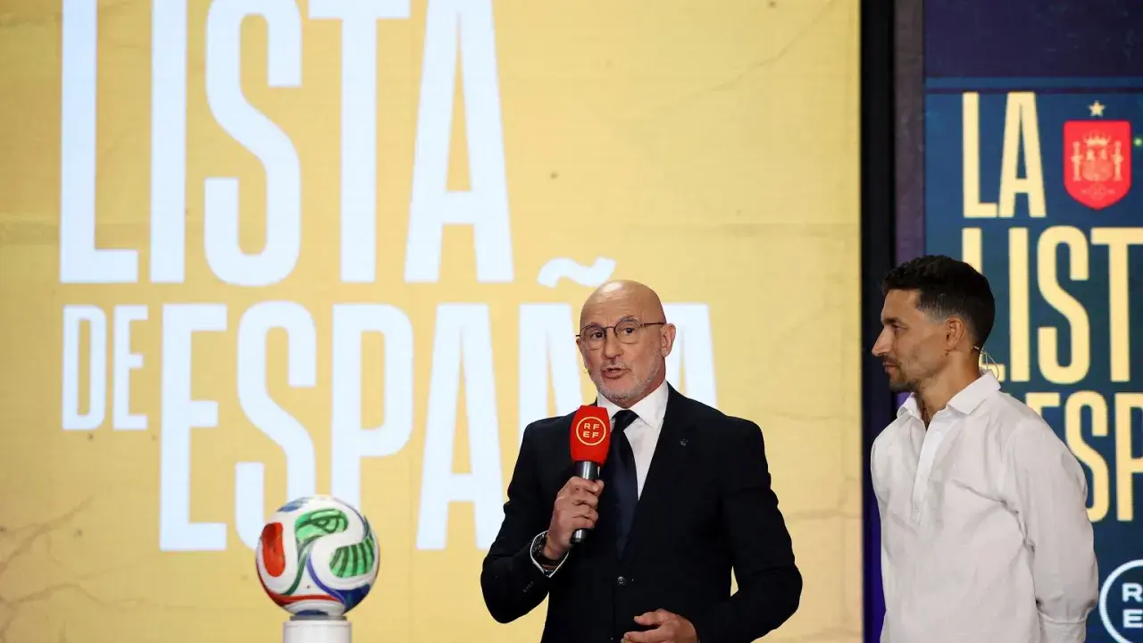 Mężczyzna w garniturze ogłasza hiszpania powołania, obok stoi piłkarz. Na ekranie w tle napis "LISTA DE ESPAÑA".