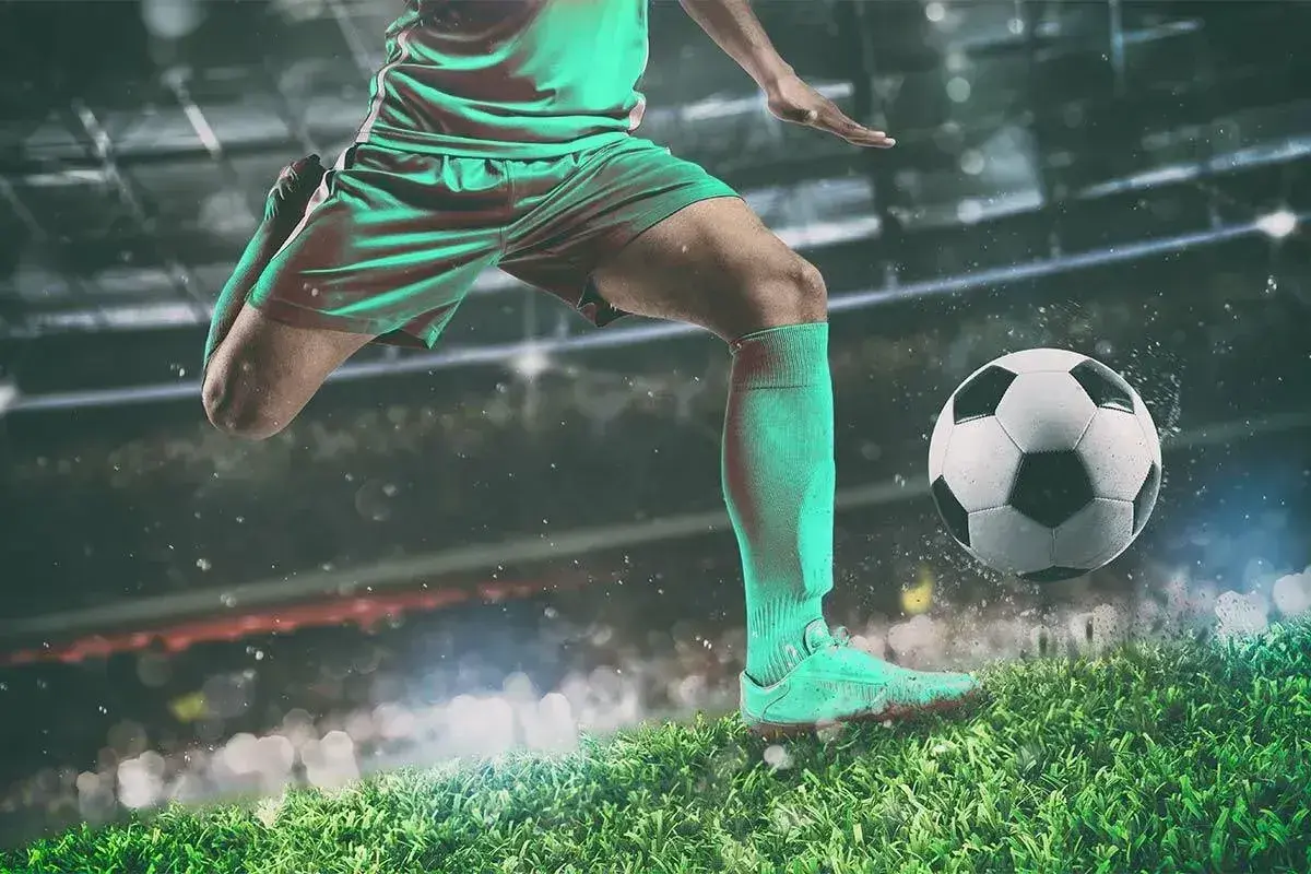 Piłkarz w akcji, jak legenda futbolu, kopie piłkę na tle stadionu.