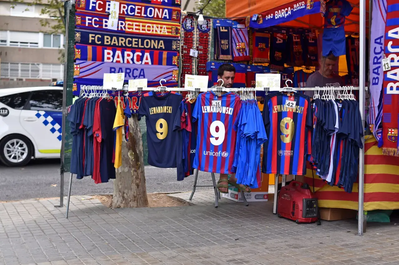 Stoisko z gadżetami FC Barcelona, w tym koszulkami z nazwiskiem Lewandowskiego. W tle widać radiowóz. Polacy w La Liga to już rzeczywistość!