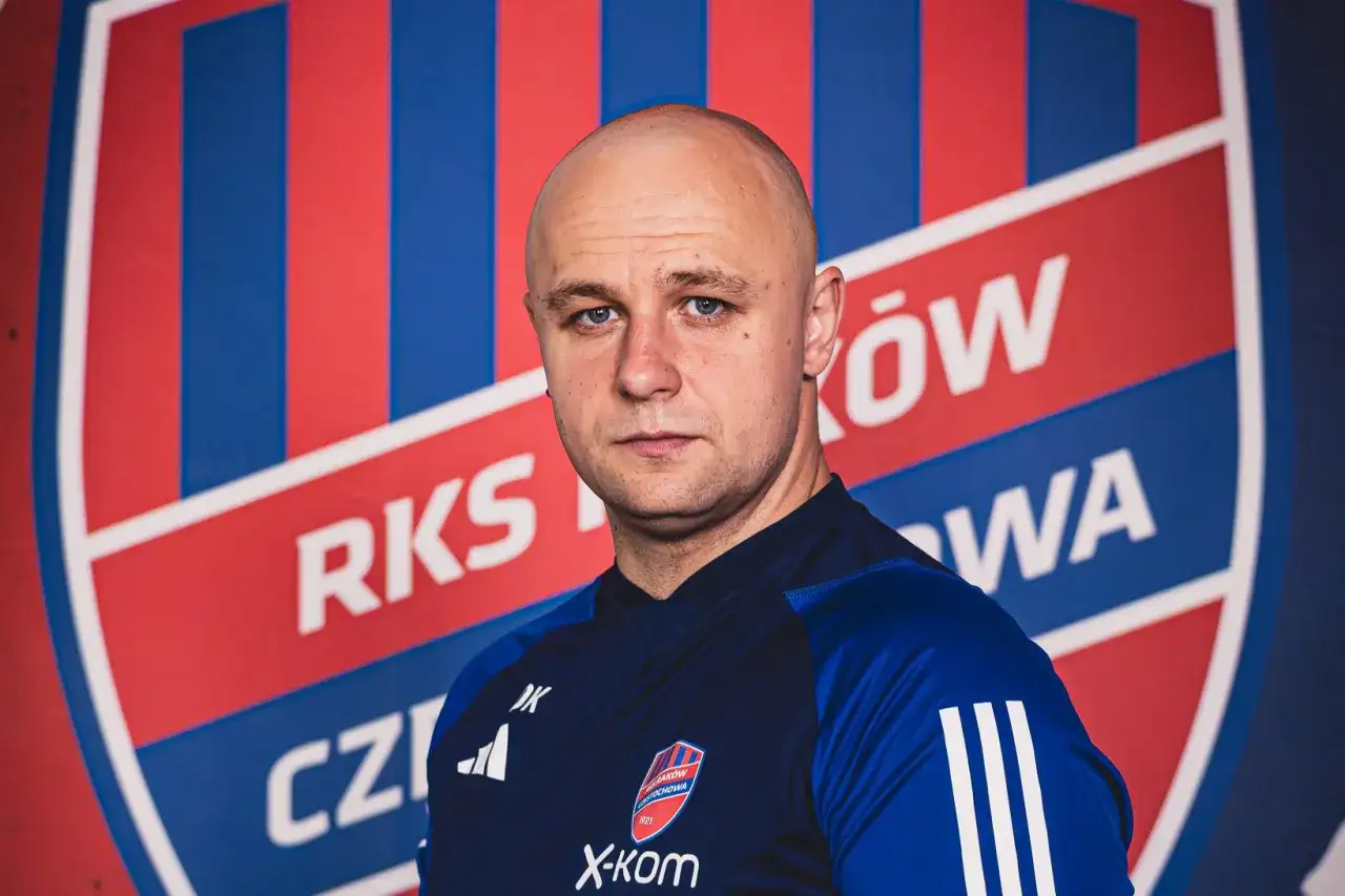 Łysy mężczyzna, trener Rakowa, patrzy prosto przed siebie na tle klubowego herbu.