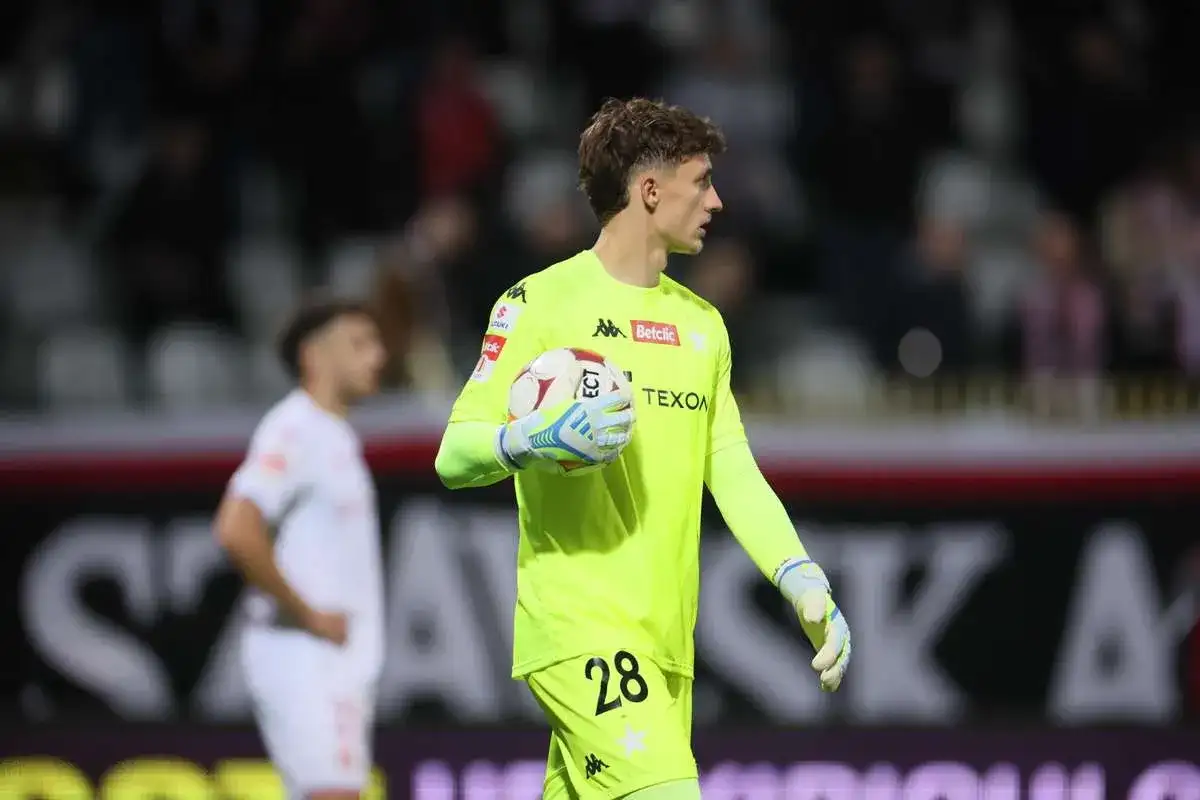 Młody bramkarz Wisły Kraków w neonowożółtej koszulce z numerem 28 trzyma piłkę.