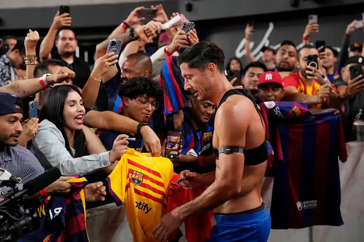 Robert Lewandowski rozdaje autografy na koszulkach FC Barcelona. Fani z telefonami w rękach dokumentują to wydarzenie.