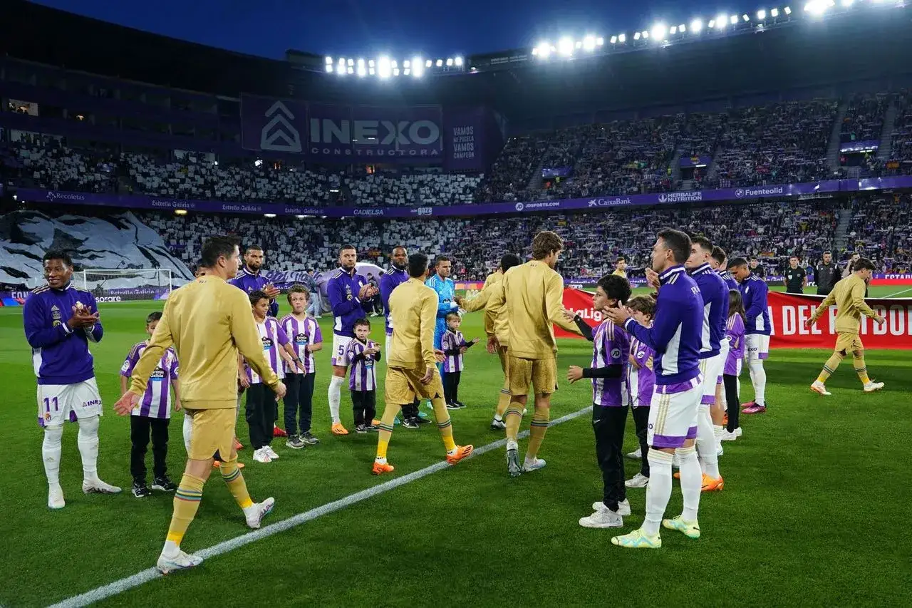 Piłkarze FC Barcelona i Valladolid na murawie stadionu. Młodzi kibice w strojach drużyn tworzą szpaler.