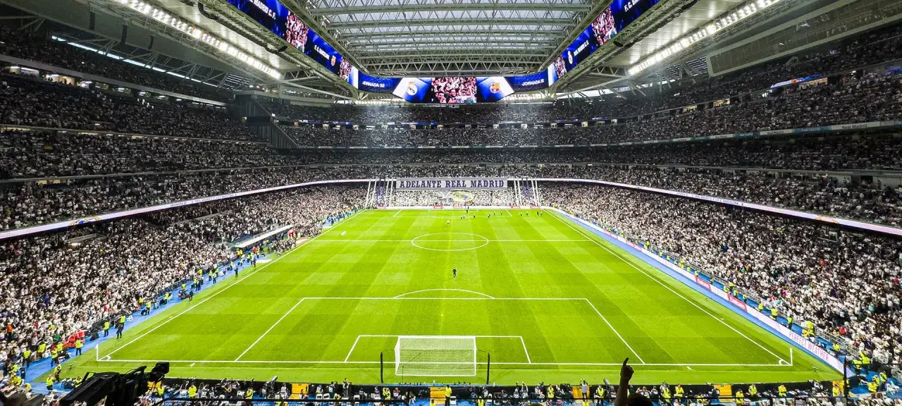 Stadion Santiago Bernabéu wypełniony kibicami, zielona murawa i baner 
