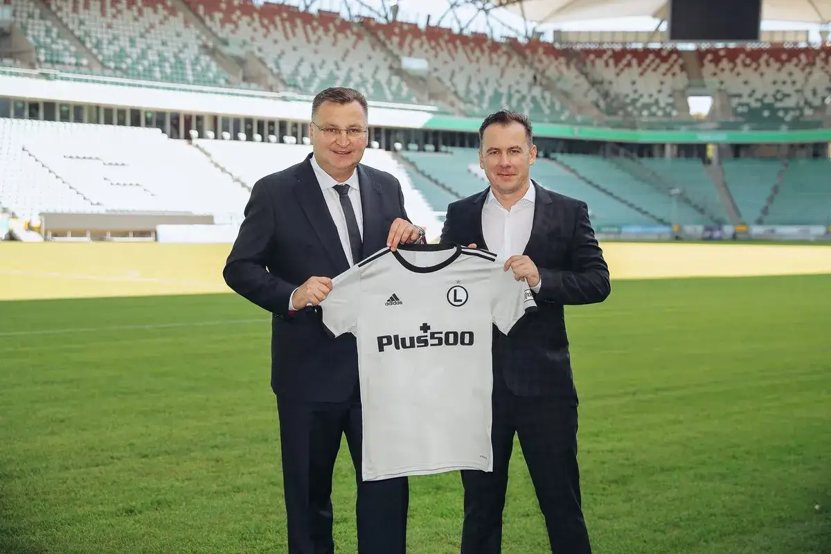 Michniewicz i przedstawiciele Legii prezentują nową koszulkę na tle stadionu.