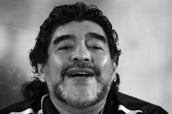 Uśmiechnięty Diego Maradona, którego zdjęcie budzi pytania: czy Diego Maradona żyje? Ikona futbolu z charakterystyczną fryzurą i zarostem.